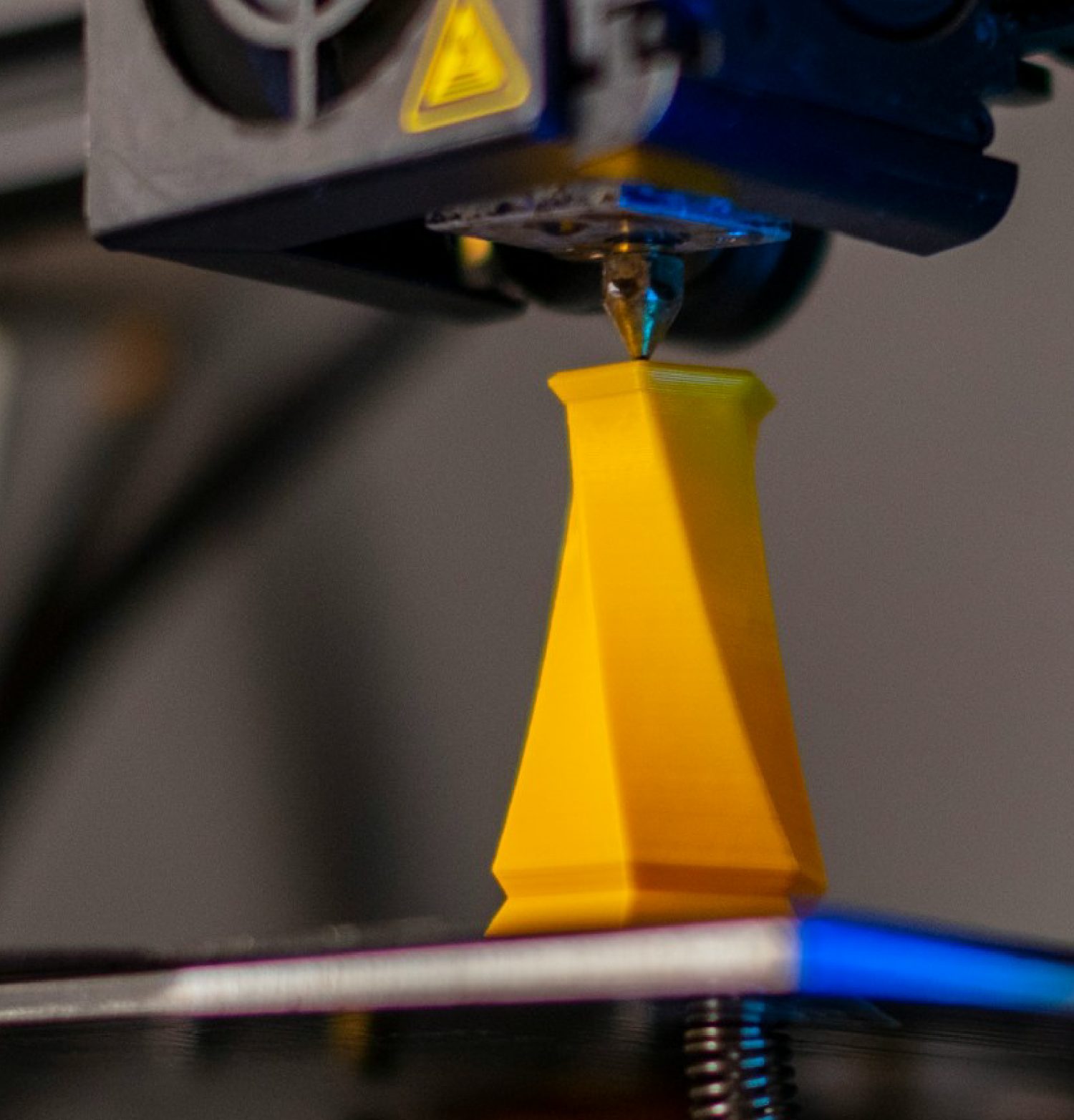 Impresora 3D fabricando una miniatura amarilla de Atlas